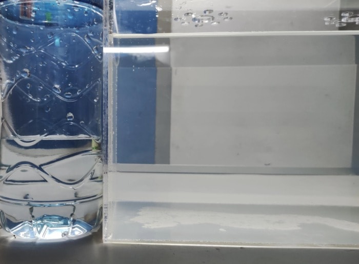 A bottle of clear mineral water sitting next to a tank with somewhat cloudy water for comparison