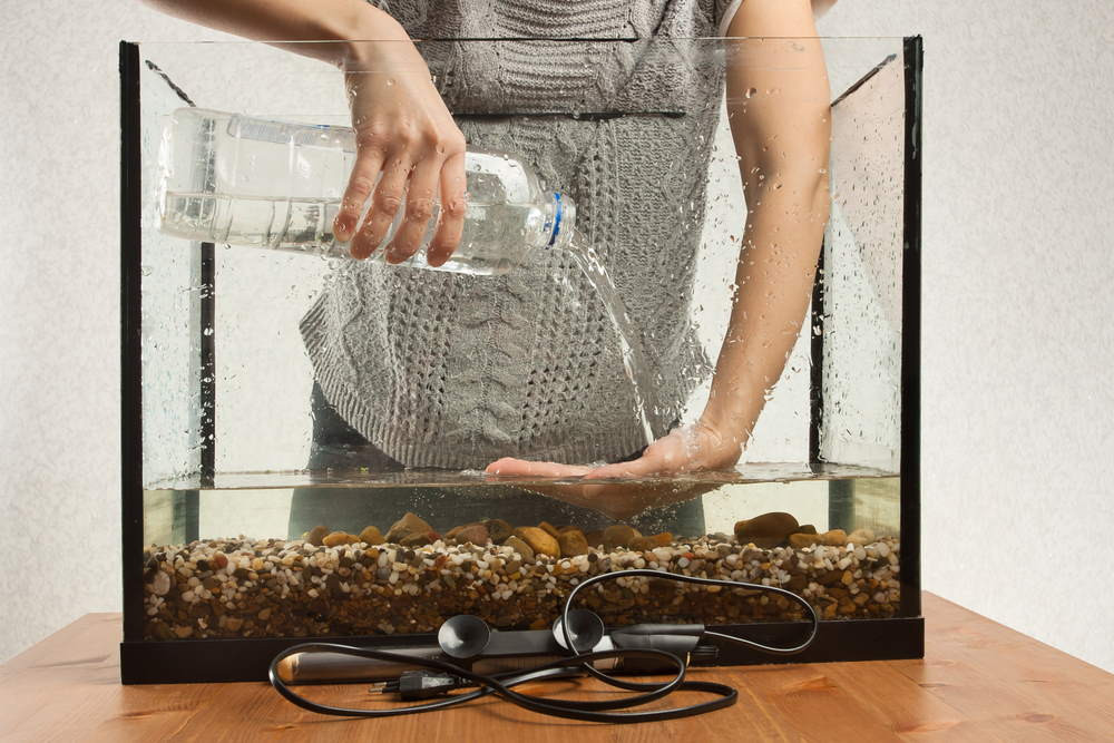 A fishkeeper using one hand to disperse water she is pouring into the container with the other hand so as not to disturb the gravel substrate.